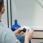 Eine Person sitzt und h&auml;lt dabei einen DualSense-Controller in der Hand.