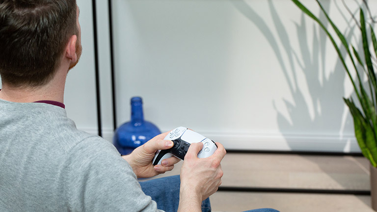 Eine Person sitzt und hält dabei einen DualSense-Controller in der Hand.