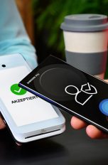 Ein Smartphone wird an ein Kartenlesegerät für einen kontaktlosen Bezahlvorgang gehalten.