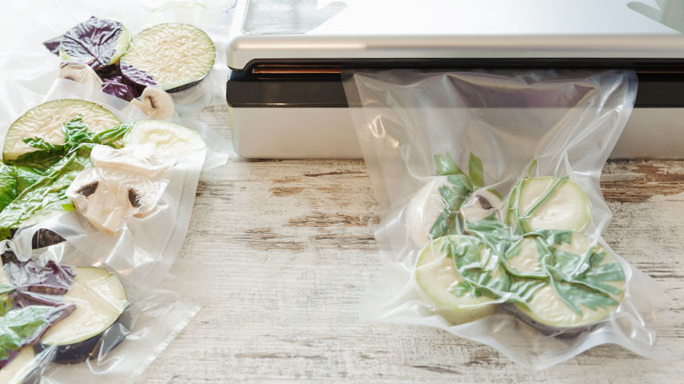 Raw vegetables and mushroom in vacuum package. Sous-vide, new technology cuisine. In ein Vakuumiergerät ist ein Plastikbeutel mit Gemüse eingelegt, das Vakuum wird gerade erzeugt.