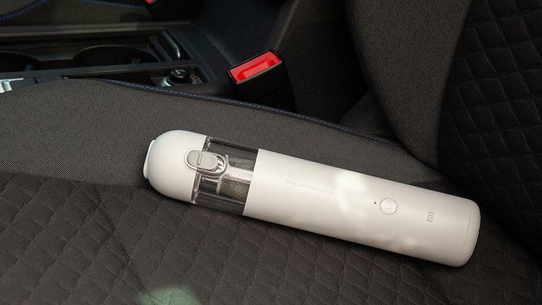 Der Xiaomi Mi Vacuum Cleaner Mini liegt auf einem Autositz mit Stoff-Bezug.