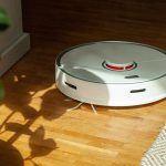 Ein Roborock S5 Max f&auml;hrt &uuml;ber einen Holzboden auf eine Topfpflanze zu.