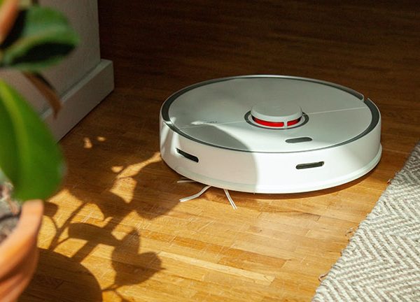 Ein Roborock S5 Max fährt über einen Holzboden auf eine Topfpflanze zu.