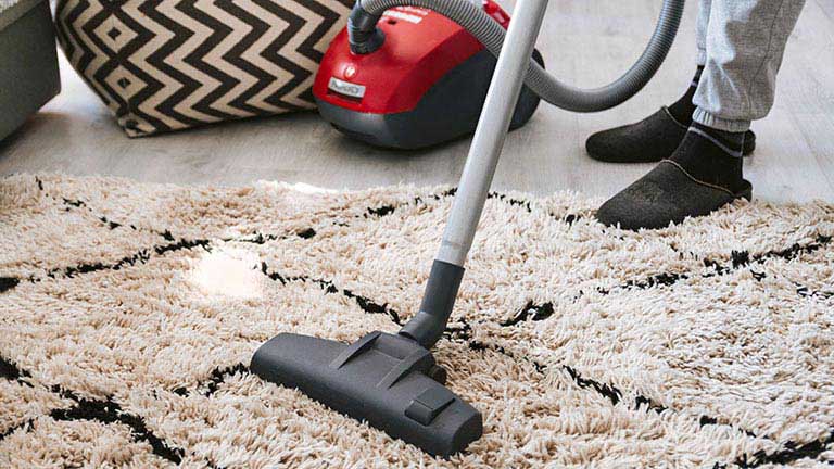 Eine Person saugt mit einem Staubsauger &uuml;ber einen flauschigen Teppich.