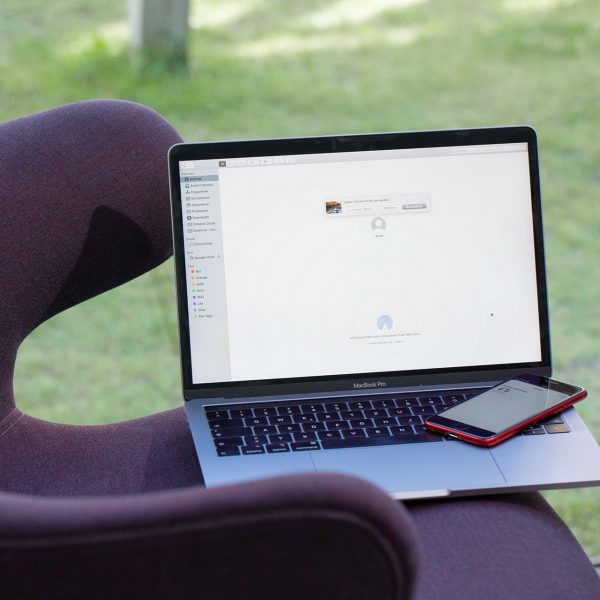 Ein MacBook Pro und ein iPhone SE auf einem Sessel. Die Geräte tauschen gerade Daten per AirDrop aus.