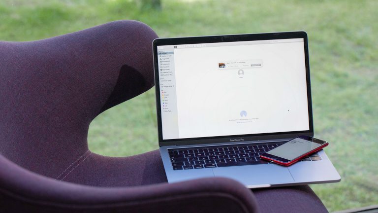 Ein MacBook Pro und ein iPhone SE auf einem Sessel. Die Geräte tauschen gerade Daten per AirDrop aus.