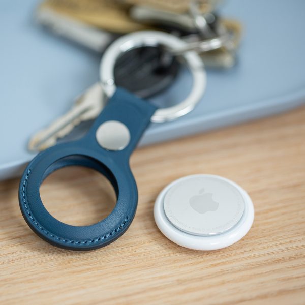 Ein Apple AirTag liegt neben einem Schl&uuml;sselanh&auml;nger. Im Hintergrund sind ein paar Euro-M&uuml;nzen f&uuml;r den Gr&ouml;&szlig;envergleich zu sehen.)