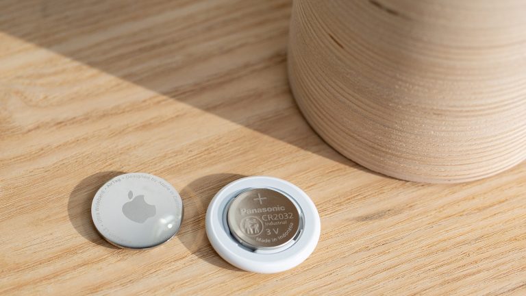 Ein geöffneter Apple AirTag, in dem die Knopfzelle zu sehen ist. Der silberne Deckel liegt daneben.