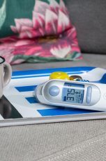 Braun ThermoScan 7 Auf einem Tablett steht eine Emailletasse mit Tee, daneben liegt ein Infrarotfieberthermometer.