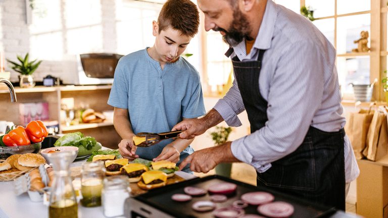 Ein Kind und eine erwachsene Person bereiten Burger vor, die sie zuvor auf einem Elektrogrill zubereitet haben.