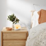 Der Google Nest Hub steht auf einem Nachttisch neben einem Bett.