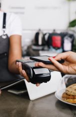 Eine Person hält ein Smartphone über ein Kartenlesegerät, um kontaktlos zu bezahlen.