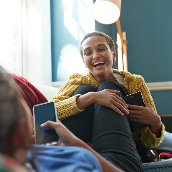Zwei Personen sitzen auf einem Sofa, beide halten ihr Smartphone in der Hand.