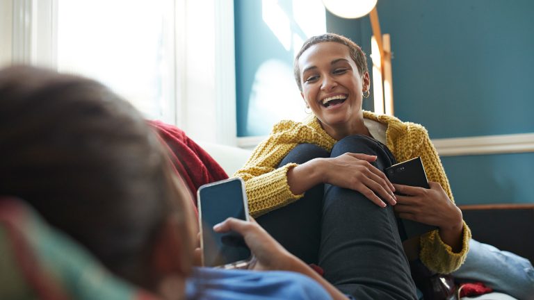 Zwei Personen sitzen auf einem Sofa, beide halten ihr Smartphone in der Hand.