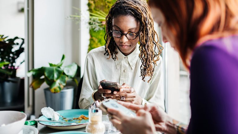 Zwei Personen sitzen an einem Esstisch und bedienen ihre Smartphones.