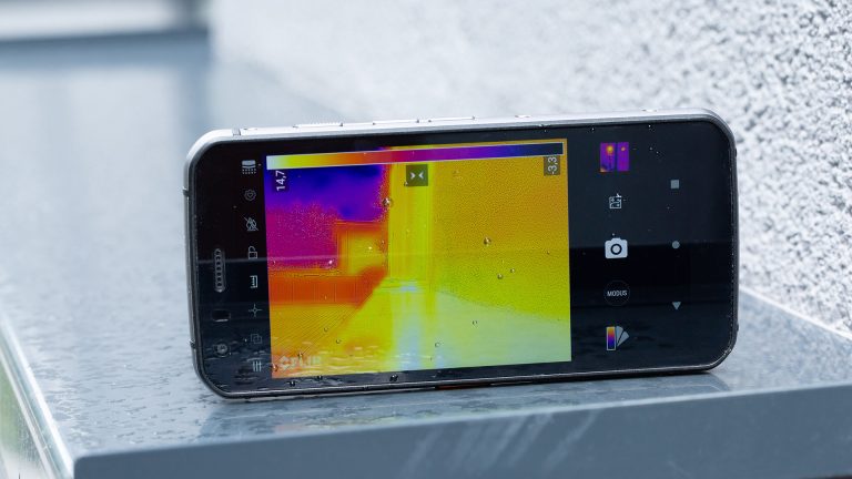 Auf dem Outdoor-Smartphone Cat S62 Pro ist die Wärmebildkamera-App geöffnet. Sie ist draußen auf eine Hauswand gerichtet, die im Bild der Kamera orange gefärbt ist.