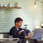 Eine Person sitzt an einem Esstisch und schaut auf einen Laptop.
