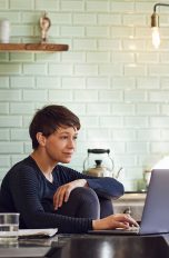 Powerline Adapter Eine Person sitzt an einem Esstisch und schaut auf einen Laptop.