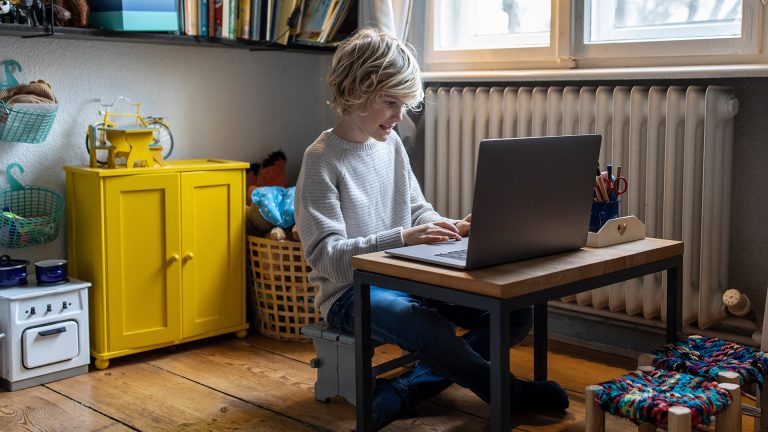 Ein Kind sitzt in seinem Zimmer vor einem Laptop.