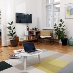 Blick in ein Wohnzimmer mit einem MacBook auf dem Couchtisch und einem Fernseher an der Wand.