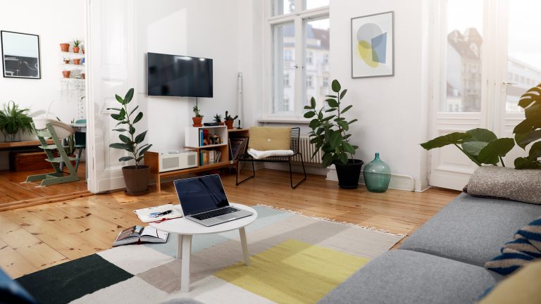 Blick in ein Wohnzimmer mit einem MacBook auf dem Couchtisch und einem Fernseher an der Wand.