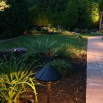 In einem illuminiertem Garten führt ein gepflasterter Weg zu einem Pavillon.