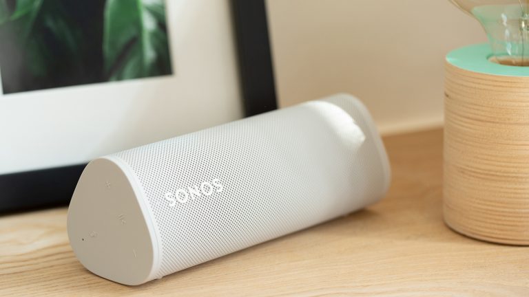 Ein Sonos Roam Lautsprecher liegt horizontal auf einer Ablagefläche. Daneben steht eine dekorative Lampe.