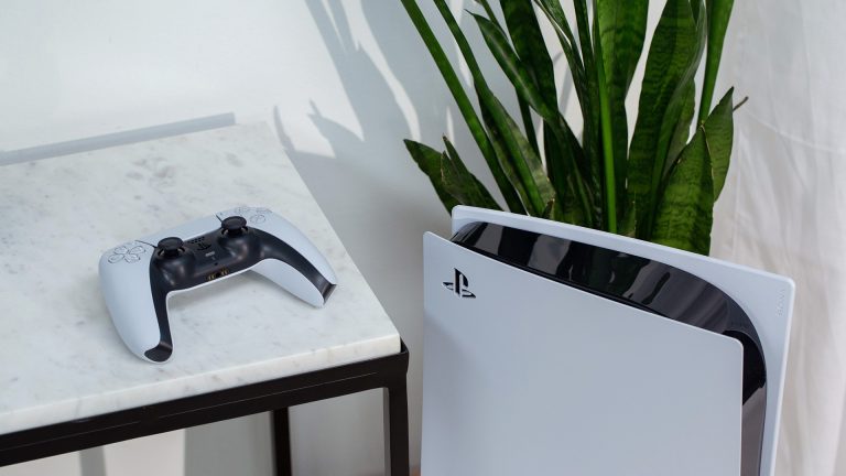 Die PlayStation 5 steht vor einer Dekopflanze. Daneben liegt der DualSense-Controller erhöht auf einem Tisch.