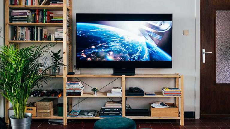 Ein Fernseher steht auf einem Holzregal. Auf dem Display läuft gerade ein Spielfilm an.