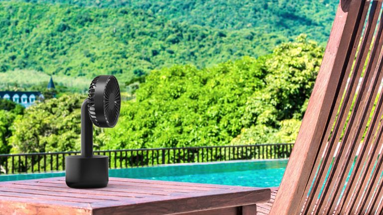 Der Akku-Ventilator von CSL steht auf einem Tisch mit Blick auf einen Außen-Pool und die Natur.
