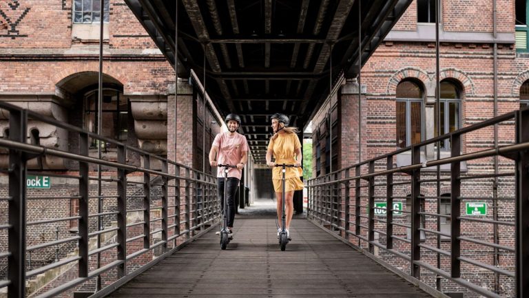 Zwei Personen fahren mit zwei KickScooter Max G30D II über eine Brücke in der Hamburger Speicherstadt.
