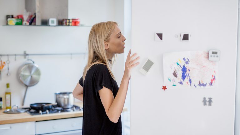 Eine Frau steht in einer Küche und schaut in einen geöffneten Kühlschrank.