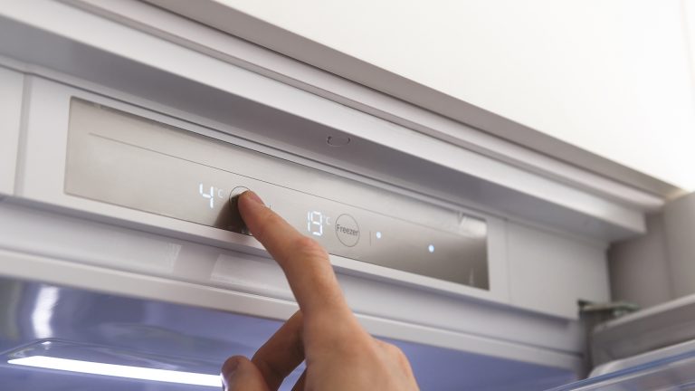 Ein ausgestreckter Zeigfinger tippt auf das Bedienfeld eines geöffneten Kühlschranks, um die Temperatur zu regulieren.