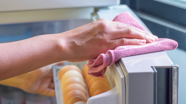 Eine Person wischt mit einem Tuch über die obere Kante einer Kühlschranktür.