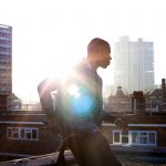 Eine Person lehnt auf einem Fahrrad, das auf einem Hausdach steht. Die Sonne scheint ins Bild und erzeugt einen Lens-Flare-Effekt.