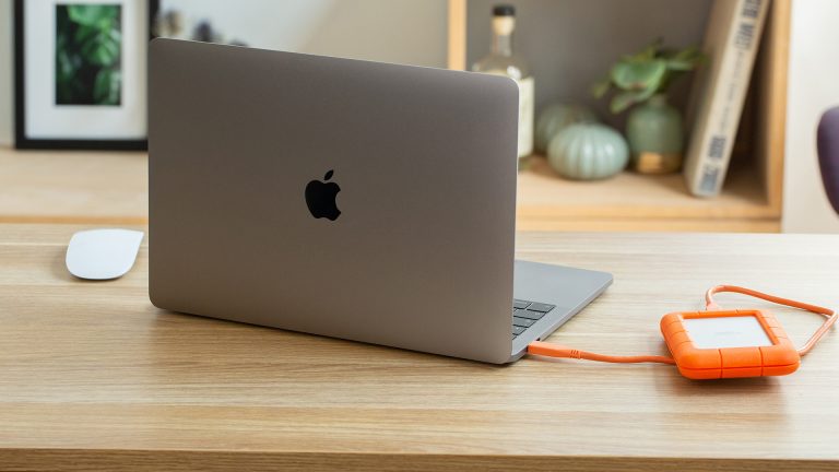 Ein aufgeklapptes MacBook steht auf einem Schreibtisch. Daneben liegt eine angeschlossene, externe Festplatte.