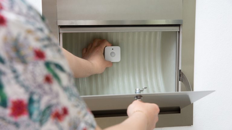 Eine Person befestigt einen Philips Hue Bewegungsmelder in einem Hausbriefkasten.