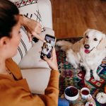 Eine Frau richtet ihr Smartphone auf ihren Hund, der vor ihr auf dem Teppich sitzt. Auf ihrem Smartphone stellt sie das Motiv scharf.