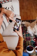 Eine Frau richtet ihr Smartphone auf ihren Hund, der vor ihr auf dem Teppich sitzt. Auf ihrem Smartphone stellt sie das Motiv scharf.