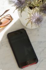 Ein Smartphone liegt auf einem Marmortisch im Schatten. Daneben liegt eine Sonnenbrille.