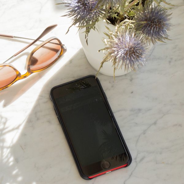 Ein Smartphone liegt auf einem Marmortisch im Schatten. Daneben liegt eine Sonnenbrille.