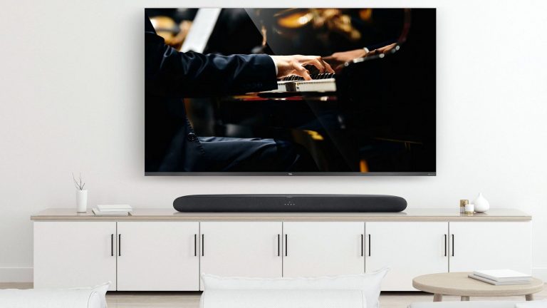 An der Wand über einem TV-Sideboard hängt ein TV-Gerät, auf dem Board steht eine Soundbar.