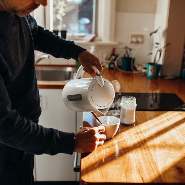 Eine Person gie&szlig;t hei&szlig;es Wasser aus einem Wasserkocher in eine Tasse.