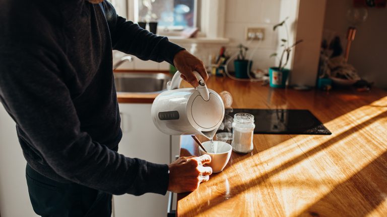 Eine Person gie&szlig;t hei&szlig;es Wasser aus einem Wasserkocher in eine Tasse.