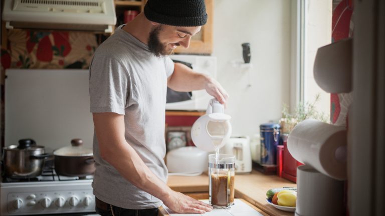 Eine Person gie&szlig;t hei&szlig;es Wasser aus einem Wasserkocher in eine French Press.
