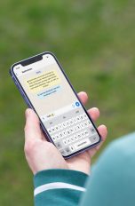 WhatsApp Broadcast Eine Person hält ein iPhone 12 in der Hand. Darauf ist der Beginn eines Chats bei WhatsApp zu erkennen.