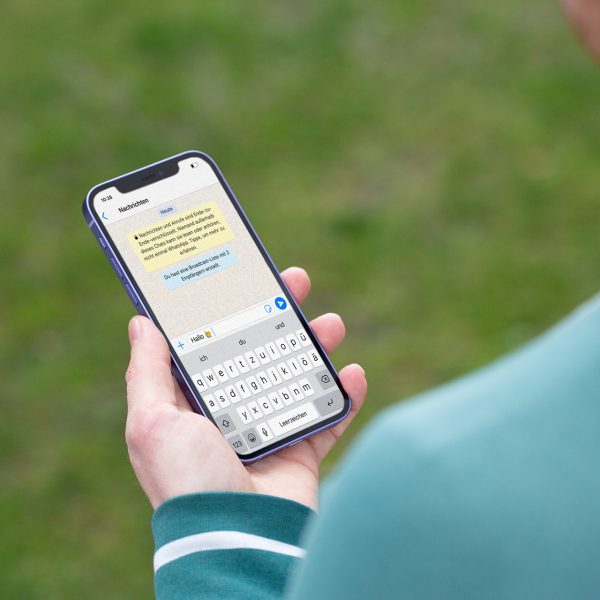 Eine Person h&auml;lt ein iPhone 12 in der Hand. Darauf ist der Beginn eines Chats bei WhatsApp zu erkennen.