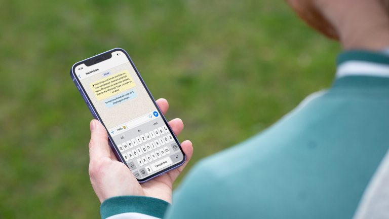 Eine Person hält ein iPhone 12 in der Hand. Darauf ist der Beginn eines Chats bei WhatsApp zu erkennen.