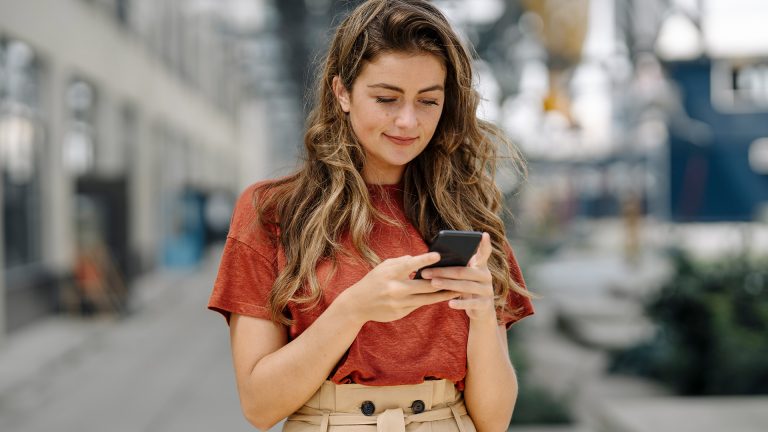 Eine junge Frau steht in einer Einkaufspassage und schaut auf ihr Smartphone.