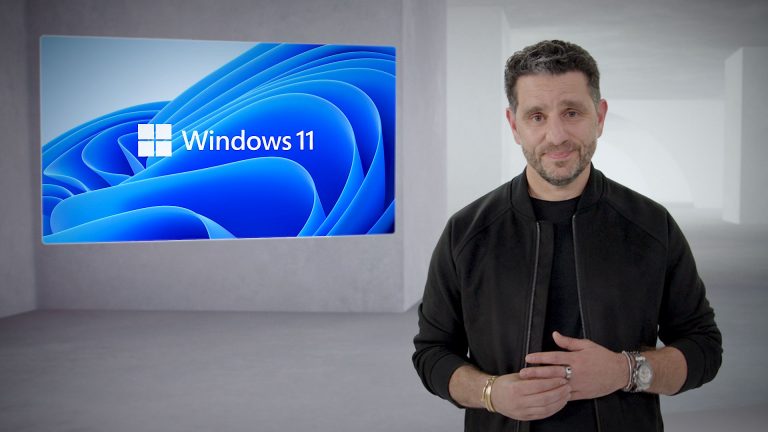 Panos Panay, Chief Product Officer bei Microsoft, steht vor der Kamera. Im Hintergrund ist das Logo von Windows 11 zu sehen.